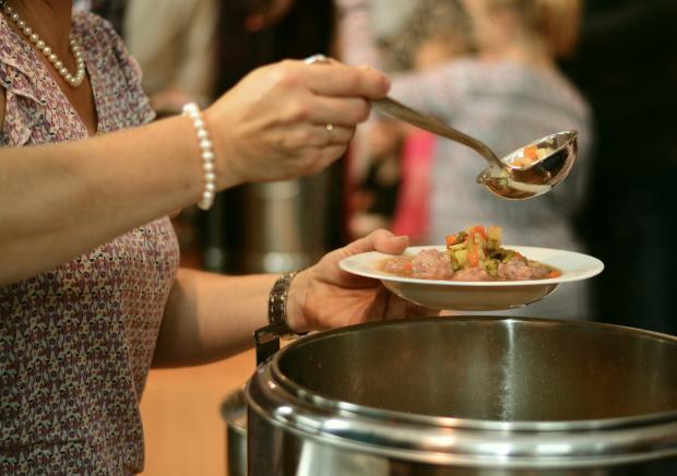 Person serving soup from large pan into bowl